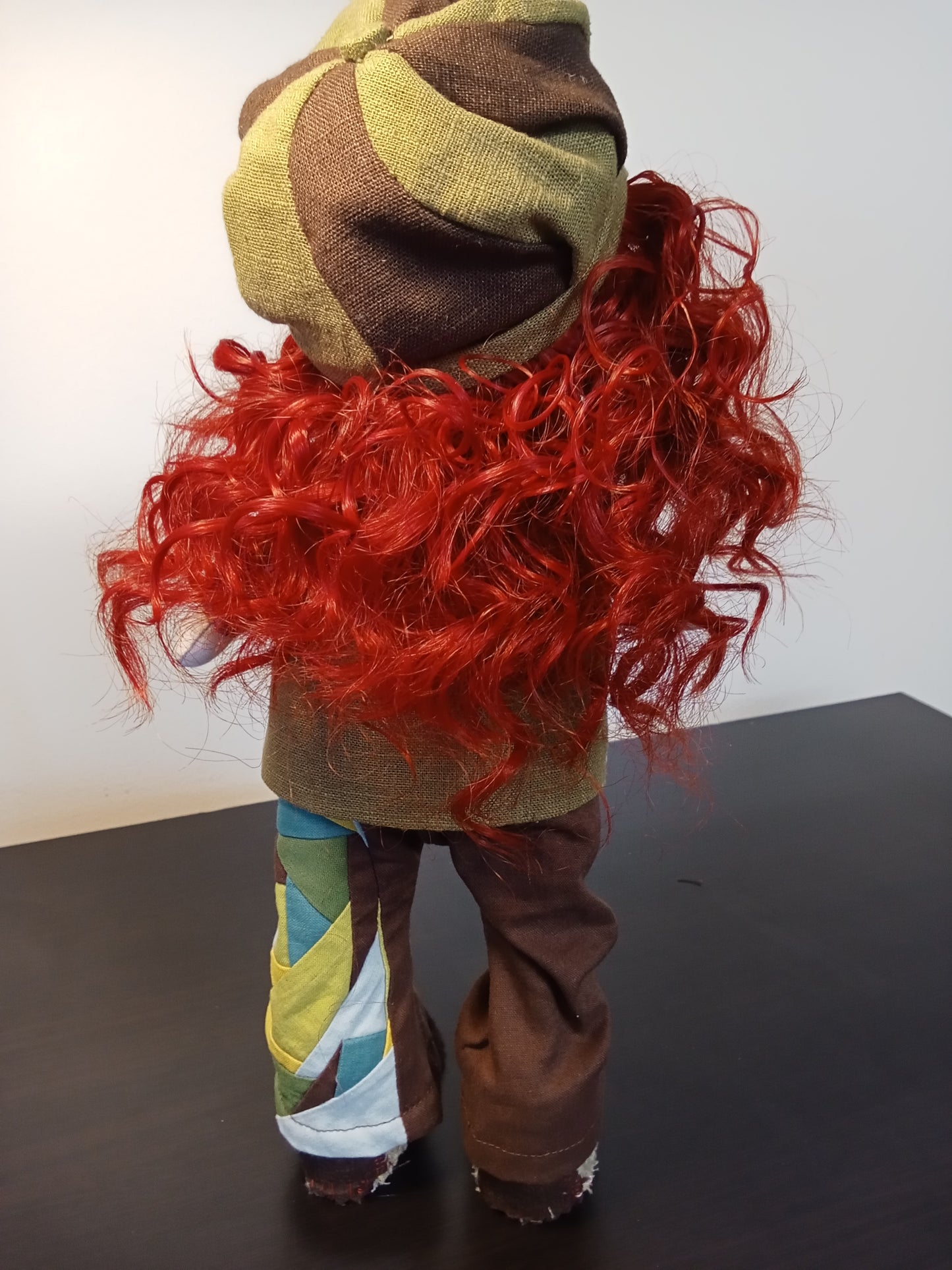 “Rear portrait of Handmade collectible doll with red curly hair wearing a colorful boho outfit.”