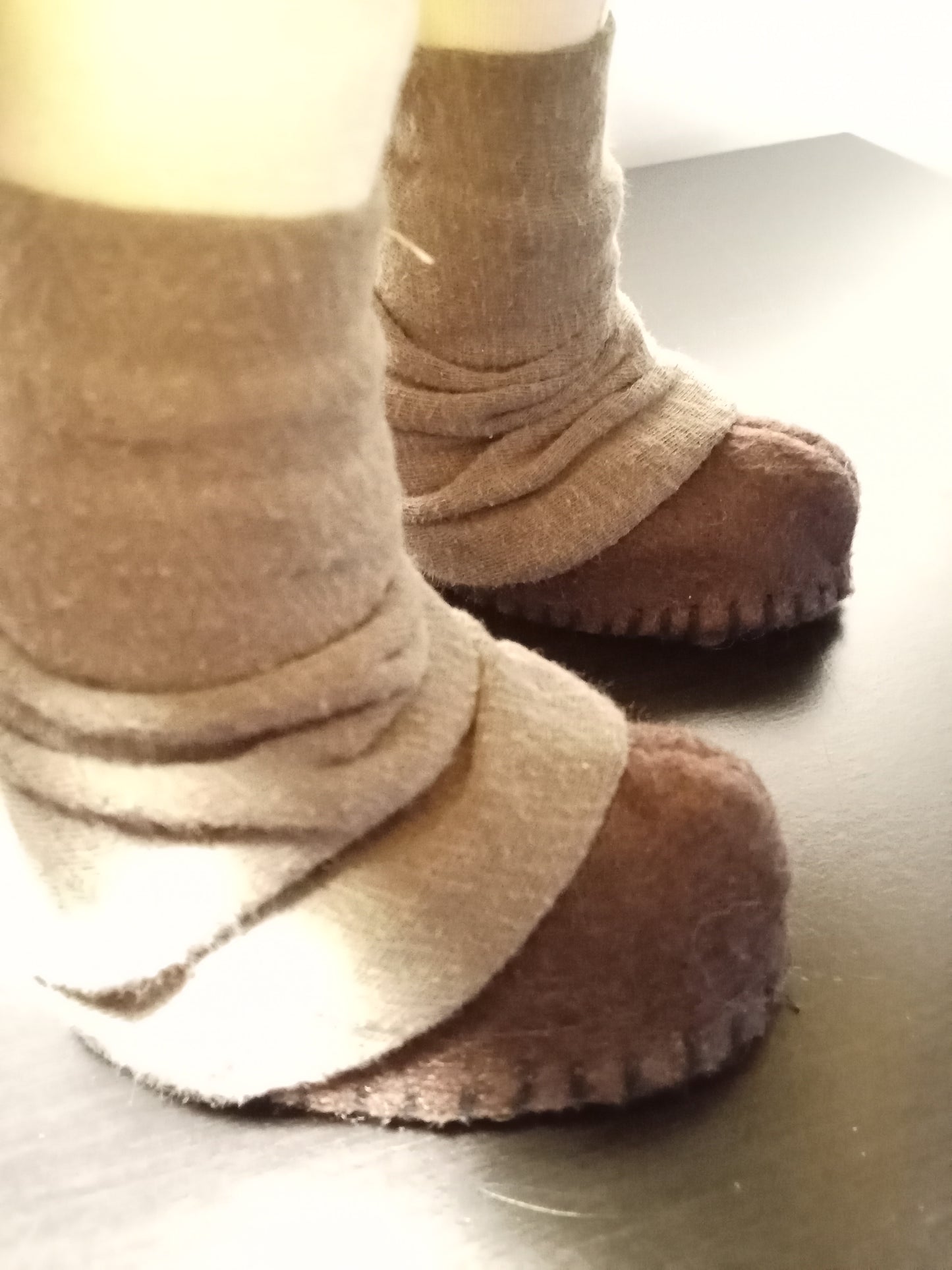 Pair of brown fuzzy slippers worn with beige socks on a dark surface. Collector edition handcrafted phirosadoll, first light collection.