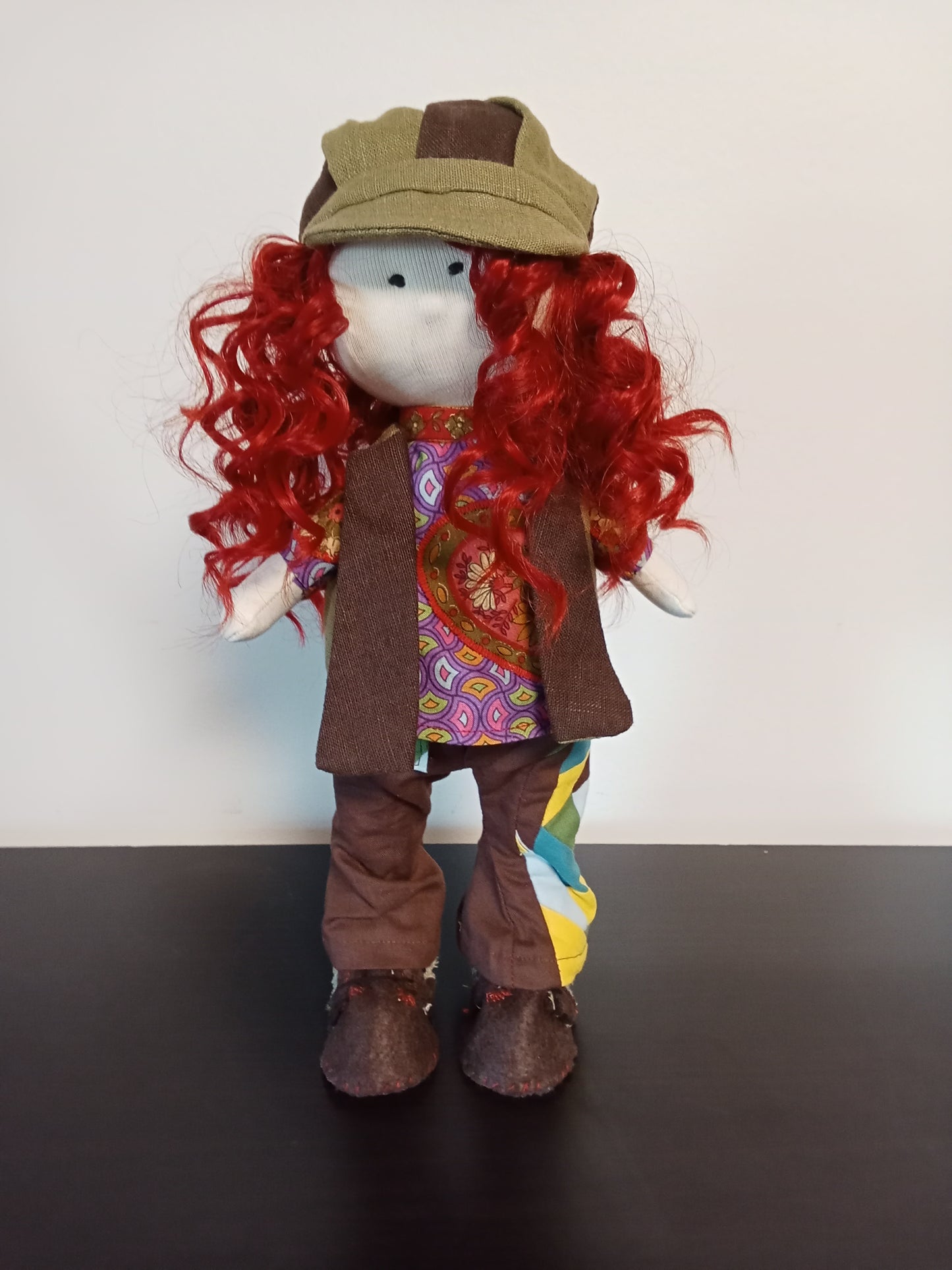 “Portrait of Handmade collectible doll with red curly hair wearing a colorful  unique outfit.”