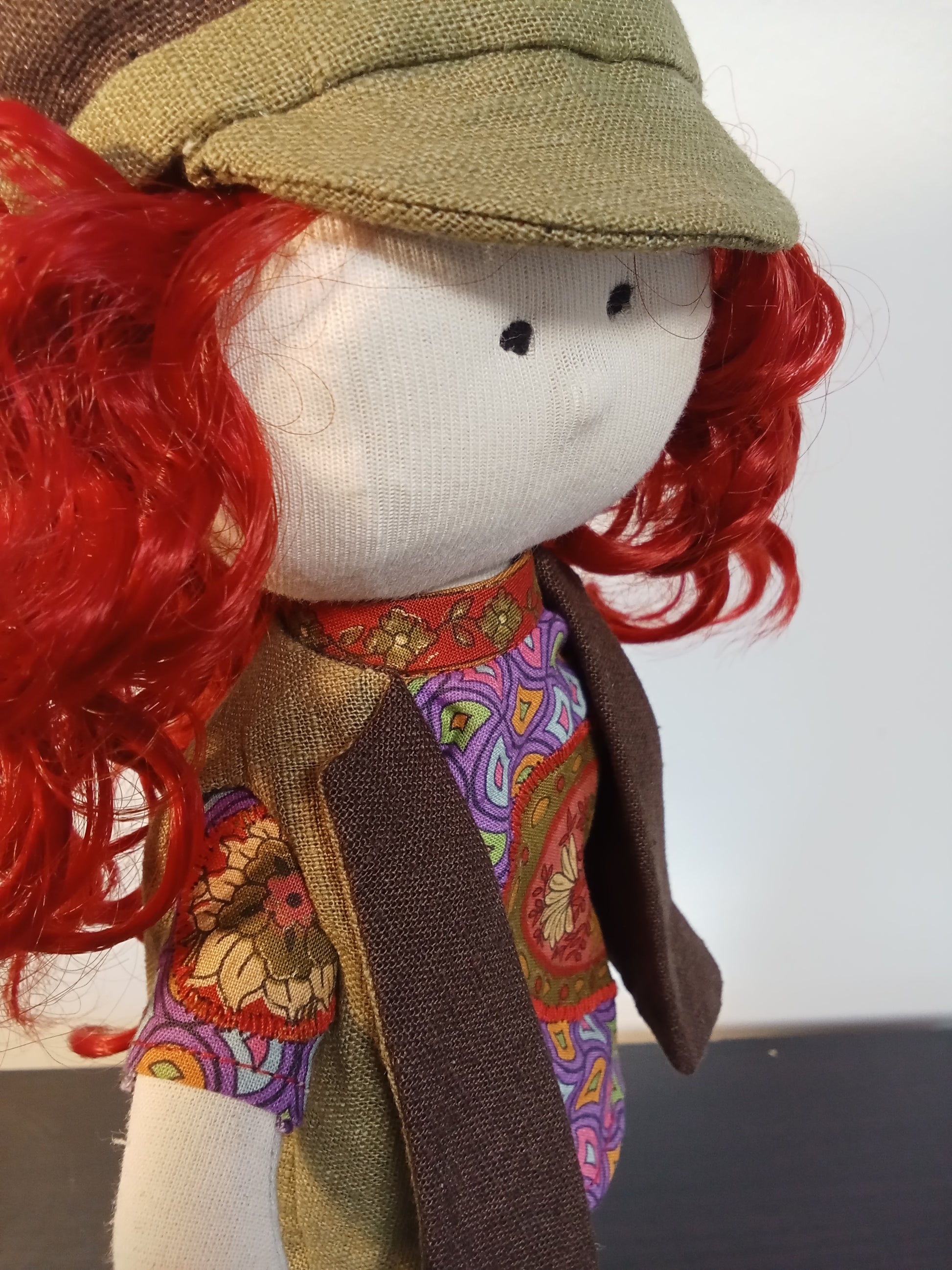“Close up side view of Handmade collectible doll with red curly hair wearing a colorful boho outfit.”